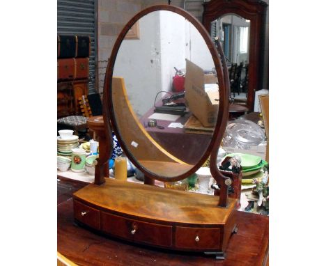 An early 19th C mahogany oval bow fronted toilet mirror, with one long and two short drawers having turned ivory handles on s