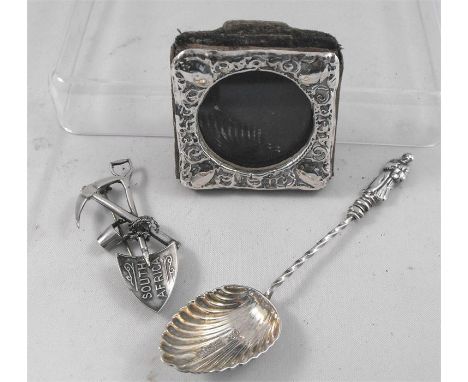 A silver photograph frame, a silver apostle spoon and  a South African silver brooch in the form of a spade and pick axe (3)