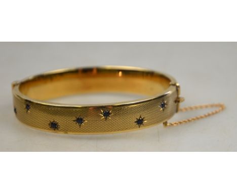 A 9ct yellow gold engine turned hinged bangle set with seven small sapphires in gypsy setting on front section, makers Cropp 