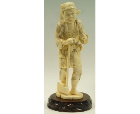 A late 19th century Japanese ivory okimono of a Woodcutter, carrying a bundle of wood and walking with axe, on a later wooden