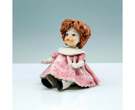 A ceramic doll that depicts a young girl seated in a pink dress with light brown string hair. Zampiva signature. Made in Ital