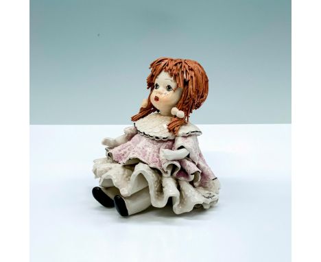 A ceramic doll that depicts a young girl seated in a purple and white dress with light brown string hair. Zampiva signature. 