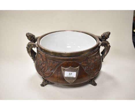 A large Victorian design carved oak punch bowl having ceramic liner and cast metal feet and handles in the form of semi nude 