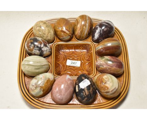 Twleve natural stone eggs, including marble and onyx, in brown glazed ceramic holder.