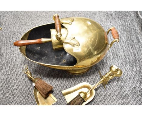 A vintage brass helmet form coal scuttle with integrated shovel and two companion sets.