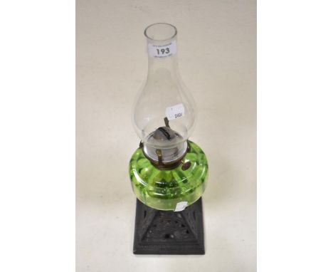 An antique oil lamp, having cast metal base and green glass reservoir.