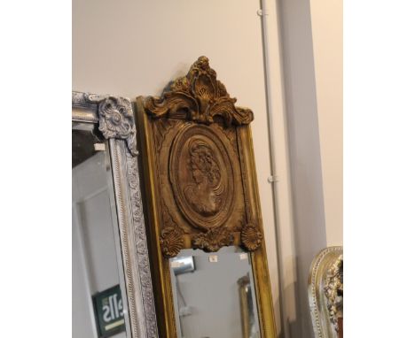 Tall and narrow gilt framed mirror, the upper section decorated with female profile carved panel, 215 cm height, 50 cm width 