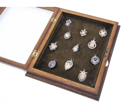 A group of eleven early 20th century silver football award fobs, presented in a wooden and glazed cabinet, some with gold pan