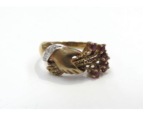 A 14ct gold ring, hands clasping a posy of flowers with ruby set to ends, diamond bracelet to wrist. Size N, 4.2g