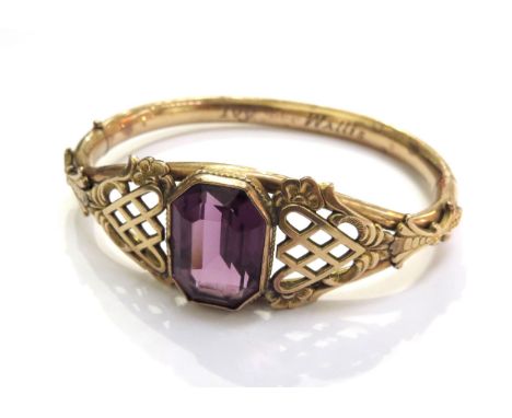 A Victorian gold filled Bates and Bacon bangle set centrally with an amethyst coloured stone with ornate scroll and openwork 