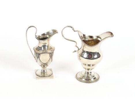 An Edwardian silver pedestal cream jug, having swag decoration, raised on a square base, London 1909; and another, London 190