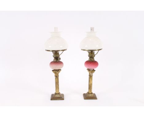 A pair of oil lamps, having fluted ruby tinted reservoirs, white opaque shades, raised on gilded corinthian columns, 47cm hig