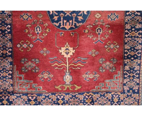 A Khotan carpet, having central medallion surrounded by stylised flowers and objects within geometric borders, on deep red an