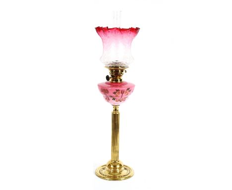A Victorian oil lamp, having frilled cranberry tinted glass shade above opaque ruby reservoir with painted floral decoration,