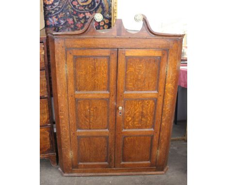 A George III oak hanging corner cupboard, surmounted by a swan arched pediment inset with brass embossed roundels, with inter