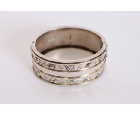 A silver snap bangle, having raised foliate decoration