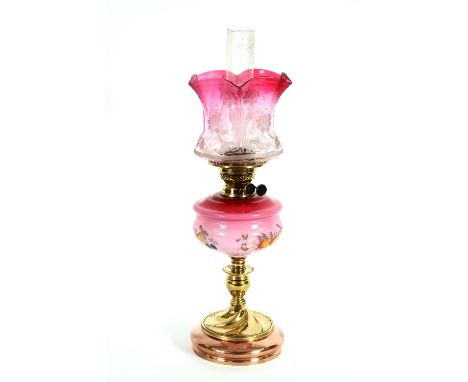 A Victorian oil lamp, having cranberry tinted shade with floral decoration, enamelled opaque ruby tinted reservoir, raised on