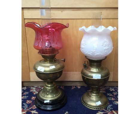 A brass Art Nouveau style brass oil lamp with cranberry coloured etched shade and another with pink opaque shade (2) 