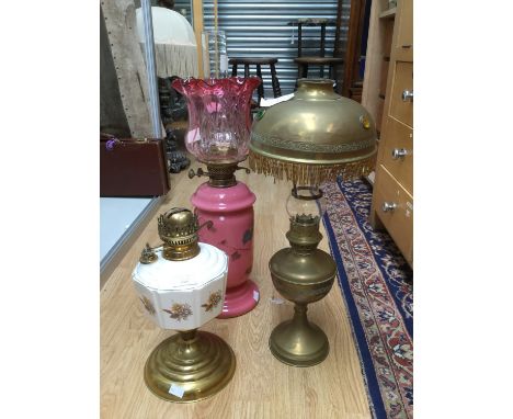 A pink glass oil lamp, floral decoration and Cranberry shade with chimney; together with a brass oil lamp with brass shade an