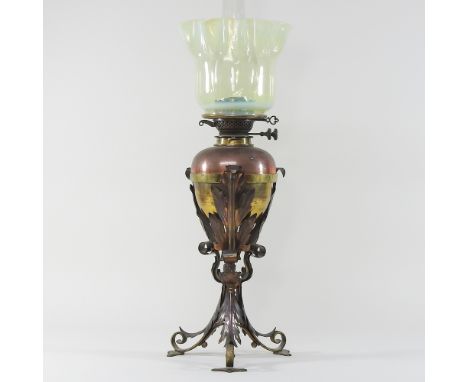 An Arts and Crafts brass and copper oil lamp, in the manner of WAS Benson, on acanthus supports, with a vaseline glass shade,