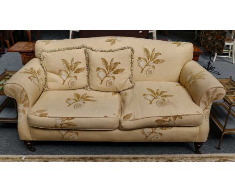 A shallow hump back three seater sofa on turned oak legs moving on castors with cream upholstery, 191cm long