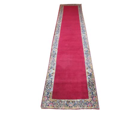KERMAN RUNNER, 535cm x 117cm, ruby open field inside a repeat palmette and scrolling vine midnight blue border.