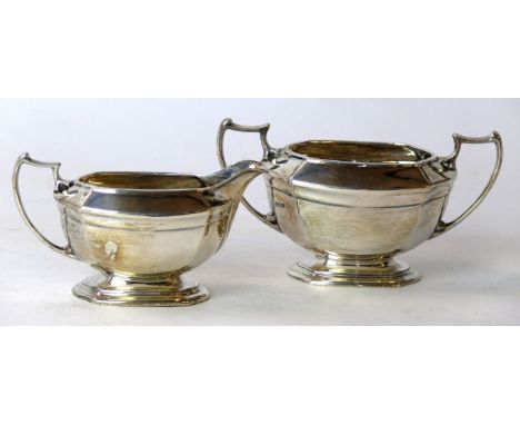 A George V silver sucrier and milk jug
Each rising from a scalloped stepped and canted base to a faceted body with high scrol