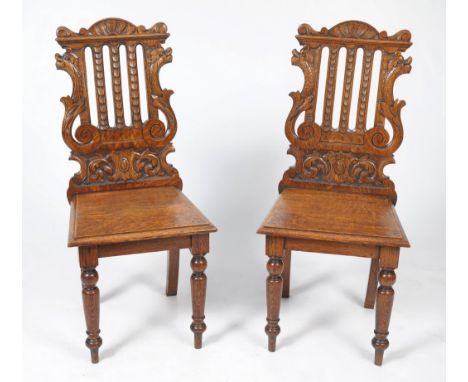 A pair of Victorian carved oak hall chairs.  Each with arched cresting rails above scale carved splats embraced by C-scroll a