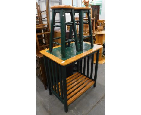 A tile top kitchen island, with slatted under tier, together with two stools with green painted bases. 