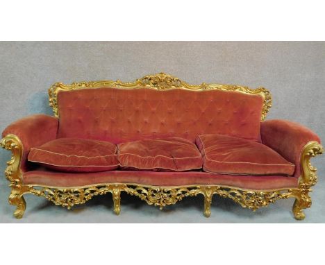 An Italian Rococo style carved giltwood sofa in buttoned rouge upholstery raised on cabriole legs. H.101 W.230 D.83cm