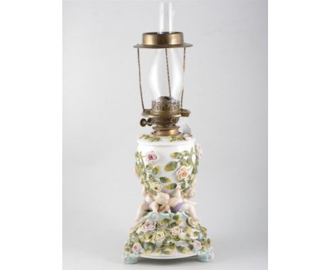 Continental porcelain oil lamp, moulded with cherubs and encrusted floral decoration, with glass chimney, 62cm.