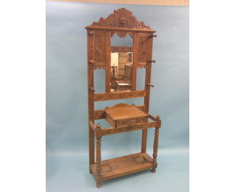 A late Victorian Flemish-style carved oak hall stand, fitted with coat-hooks, bevelled mirror, glove-drawer and stick-stands 