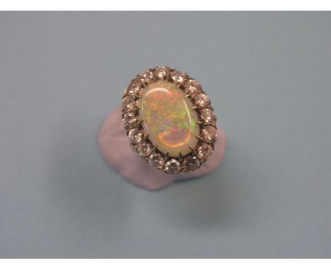 A large 18ct. gold black opal and diamond dress ring, central oval opal surrounded by sixteen claw-set diamonds