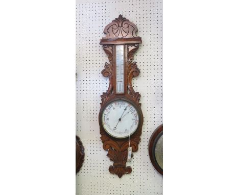 An early 20th century wheel barometer, with printed white ceramic barometer and thermometer dials, oak case carved with leafa