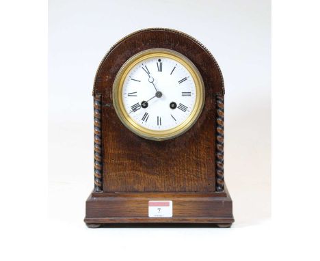 An early 20th century oak cased eight-day mantel clock, the enamelled dial showing Roman numerals, the dome topped case flank
