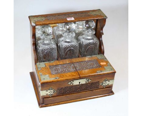 An early 20th century carved oak three-bottle tantalus, having silver plated mounts, containing three cut glass decanters, th