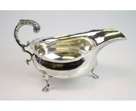Silver sauce boat, plain polished body raised on three hoof feet, scroll handle with acanthus leaf decoration, ogee style bor