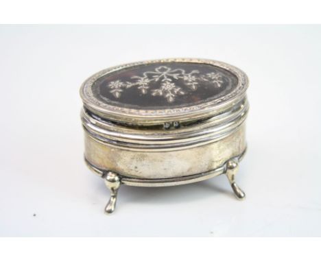 Tortoiseshell and silver oval trinket box raised on four feet, the tortoiseshell hinged lid inlaid with silver ribbon and bow