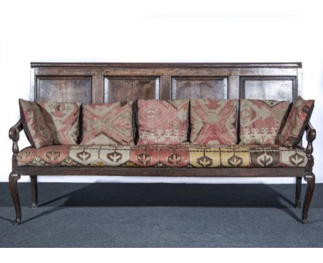 Joined oak settle, basically 18th century, moulded rail over four fielded panels, open arms, upholstered seat cushion, on cab