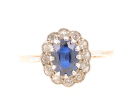 An oval cluster ring set with an oval mixed cut synthetic blue stone surrounded by twelve white stones, yellow and white meta