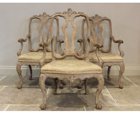 Three continental limed oak elbow chairs, 18th century, each with a pierced splat above a serpentine upholstered seat and Roc