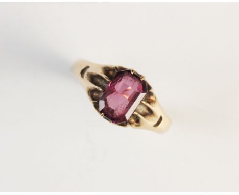 A pink garnet set ring, the central emerald cut pink garnet, within a claw setting, to the pierced shoulders and plain polish