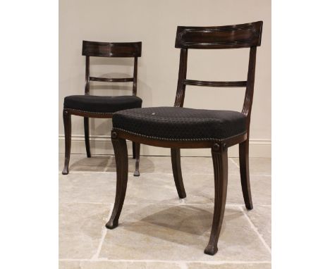 A pair of Regency mahogany dining chairs, each with a concave rail above a stuff over seat, raised upon reeded front sabre le