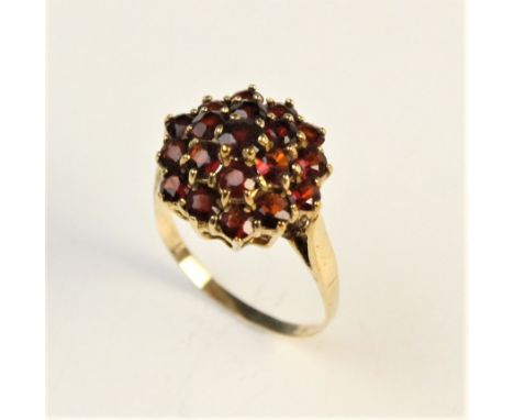 A 9ct gold garnet ring, the central garnet within a two tier surround of further garnets, all set in yellow metal, unmarked, 