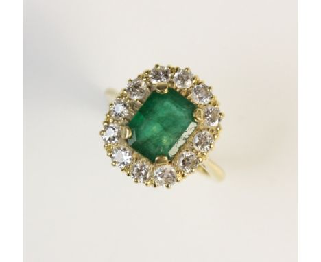 An emerald and diamond ring, the central emerald measuring 9.9mm x 7.8mm, within a four claw setting and surrounded by twelve