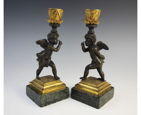 A pair of candlesticks, each with figural stem modelled as a cherub upon chequered base and marble plinth, along with a pair 