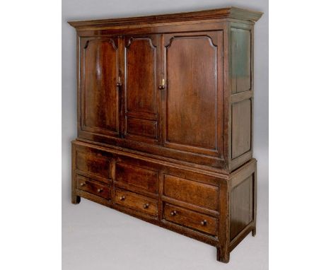 OAK LIVERY CUPBOARD, early 18th century, the pair of panelled doors flanking a matching panel on a base with three short draw