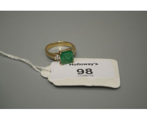 A three stone half hoop emerald and diamond ring, the square step cut emerald in four claw mount with recessed single stone b