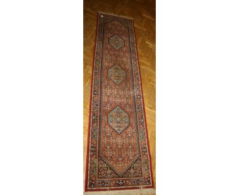 A 20th century loom woven wool runner with triple lozenge medallions on a busy largely crimson foliate ground. 292 x 70cm