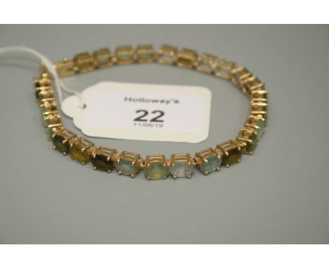 A multi gem set 18ct gold line bracelet, the mixed oval cut stones including peridot tourmaline, topaz and aquamarine, in sim
